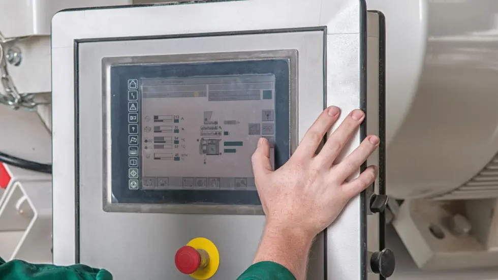 Hand operating a touchscreen control panel on industrial machinery.