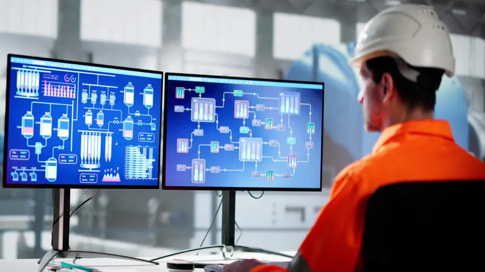 Engineer monitoring complex industrial control systems on dual screens.