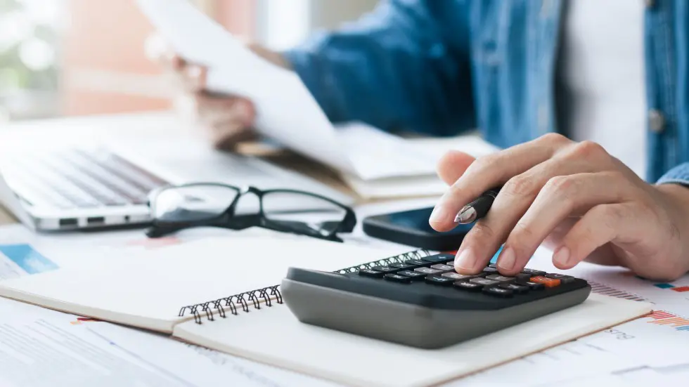 Person using a calculator and reading documents at a desk.